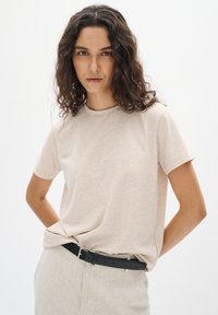 Lichtbeige T-shirt met korte mouwen van zachte stof, met een ronde hals. Gecombineerd met lichtgekleurde, op maat gemaakte broeken en een zwarte riem.