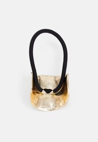 Gold metal hair tie holder with a textured finish and a black elastic band. The holder has a curved shape and a small metallic accent.