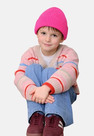 Knit pink beanie, pastel-striped cardigan, light blue jeans, and maroon athletic shoes. Child sitting with arms around knees.