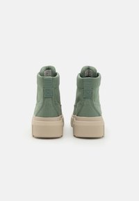 Sneakers alte verdi con tomaia in tela texture e suola in gomma beige, dotati di tallone rinforzato e linguetta sul retro per una facile calzata.