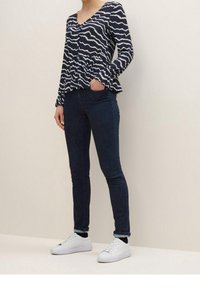 Navy and white patterned blouse with a V-neck and long, gathered sleeves, paired with dark denim skinny jeans and white sneakers.