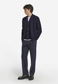 Mörkblå stickad kavaj med texturerat bladmönster, matchad med en enfärgad mörkblå väst och byxor. Skoalternativ inkluderar svarta loafers.