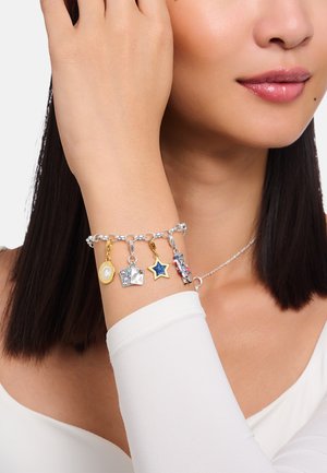 Silbernes Gliederarmband mit vier Anhängern: gelb und silbern rund, silbernes Quadrat, blauer Stern und bunter Nussknacker. Glatte Oberfläche.