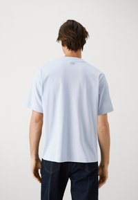 Camiseta de algodón azul claro con mangas cortas, cuello redondo y un pequeño detalle de logo en la parte posterior cerca del cuello.