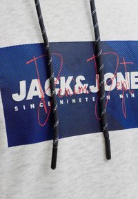 Cordons à cordon noir et blanc sur un rectangle bleu avec du texte blanc et rouge « JACK & JONES depuis mille neuf cent quatre-vingt-dix. »