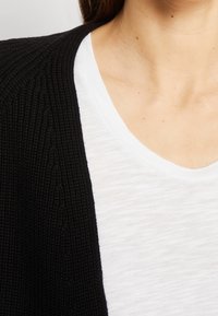 Svart texturerad cardigan i kombination med en vit, lätt crew-neck t-shirt. Fokusera p å detaljer i tyget och lager på lager.