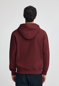 Burgundy hoodie med en texturerad yta, ribbad mudd och nederkant. Har en rymlig huva och en avslappnad passform. Enkel bakvy.