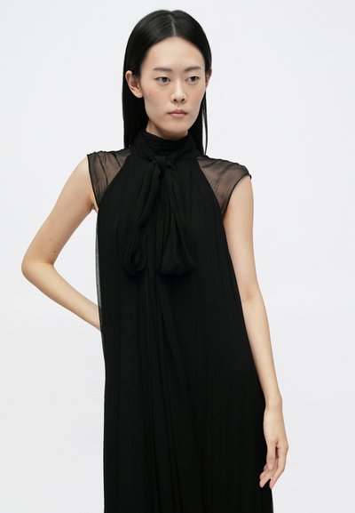 Vestido negro sin mangas con cuello alto y detalle anudado. Confeccionado en una tela liviana, presenta acentos transparentes en los hombros.