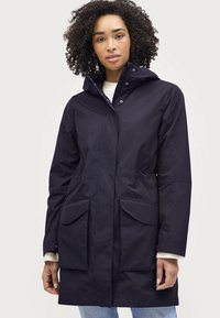 Marineblauwe waterdichte jas met een capuchon, voorzien van twee grote voorzakken, een getailleerde taille en een gladde, matte textuur.