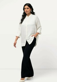 Bílá košile s límcem a bočními rozparky, spárovaná s černými rozšířenými kalhotami a béžovými podpatky. Hladké textury a uvolněný střih.