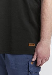 Fekete pamut póló barna bőr logóval; kék cargo shorts barna háromszög zsebfedéssel; sima textúra, laza kialakítás.