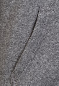 Primo piano di una tasca in tessuto grigio cucita su materiale a maglia grigio abbinato con dettagli di cucitura visibili.