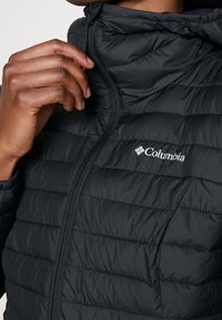 Giubbotto puffer nero con zip frontale e colletto alto. Presenta pannelli a cucitura orizzontale e un logo Columbia sul petto.