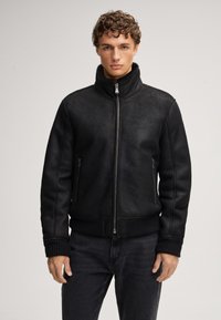 Giubbotto bomber in ecopelle nera con colletto alto, chiusura a zip sul davanti e polsini e orlo a costine. Dotato di due tasche laterali con zip e una texture liscia.