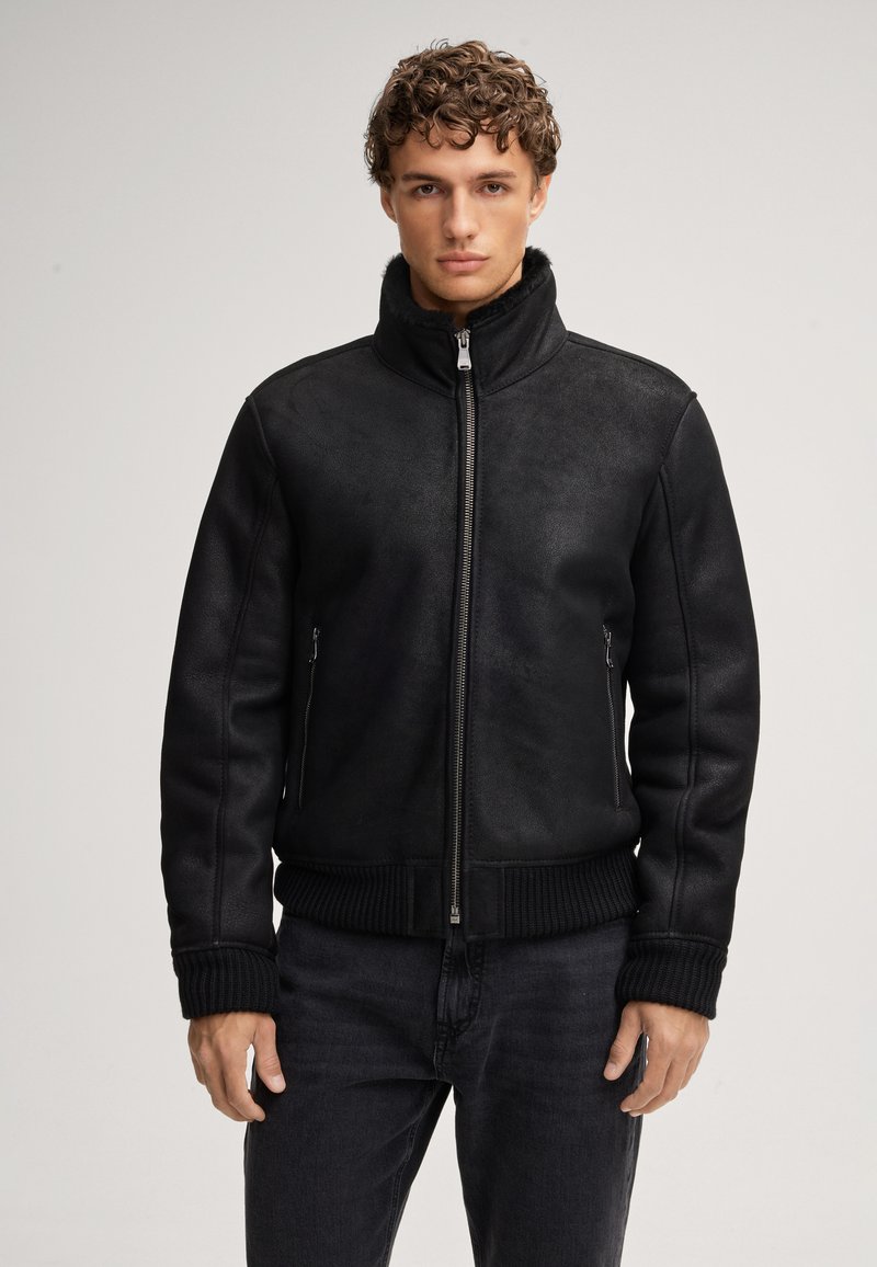 Giubbotto bomber in ecopelle nera con colletto alto, chiusura a zip sul davanti e polsini e orlo a costine. Dotato di due tasche laterali con zip e una texture liscia.