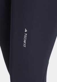Leggings fitness blu navy con una texture liscia e un design aderente. Presenta un logo bianco "TECHFIT" sul lato.