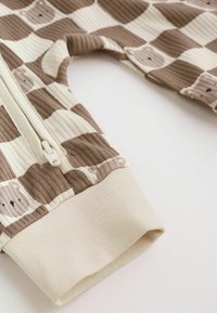 Brown and beige checkered baby romper sleeve with bear faces pattern, ribbed fabric, elastic cuff, and a white zipper.