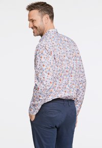 Chemise florale bleu clair avec des accents orange et turquoise, col boutonné, manches longues et coupe décontractée, associée à un pantalon navy foncé.