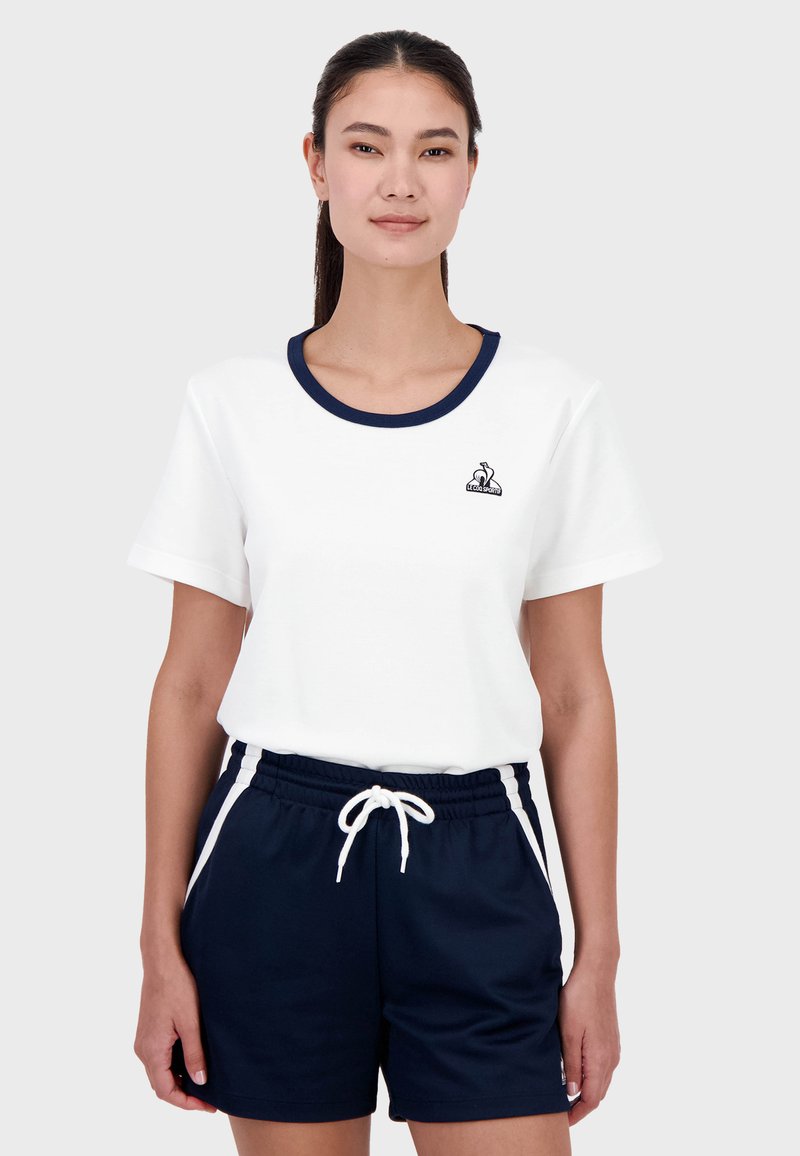 Camiseta blanca con escote en pico en navy, mangas cortas, combinada con pantalones cortos navy con cordón blanco y franjas laterales.