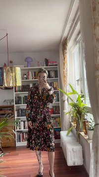 Vestido floral con un fondo negro, diseño plisado, flores rojas y amarillas vibrantes, mangas largas y escote en V.