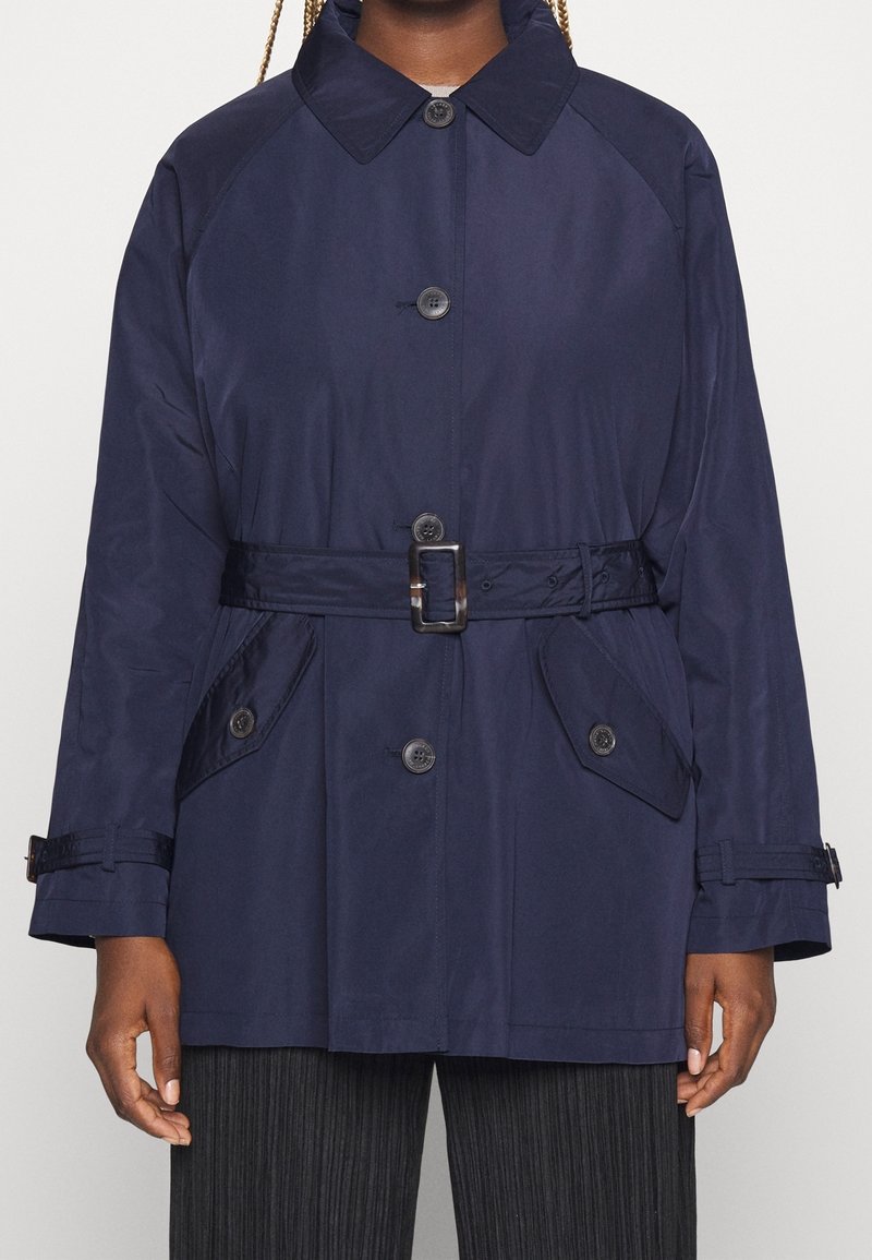 Giacca blu navy con cintura, colletto, chiusura con bottoni, tasche laterali e una texture liscia. Presenta un design strutturato con maniche raglan.