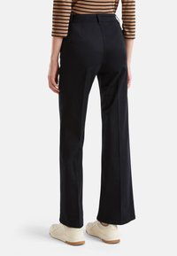 Black wide-leg trousers made of cotton with a smooth texture, featuring a high waist and back pockets, paired with white sneakers.