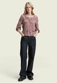 Rosa gemusterte Bluse mit Rundhalsausschnitt und elastischem Bund, kombiniert mit dunkelblauen weiten Jeans und klobigen schwarzen Schuhen.