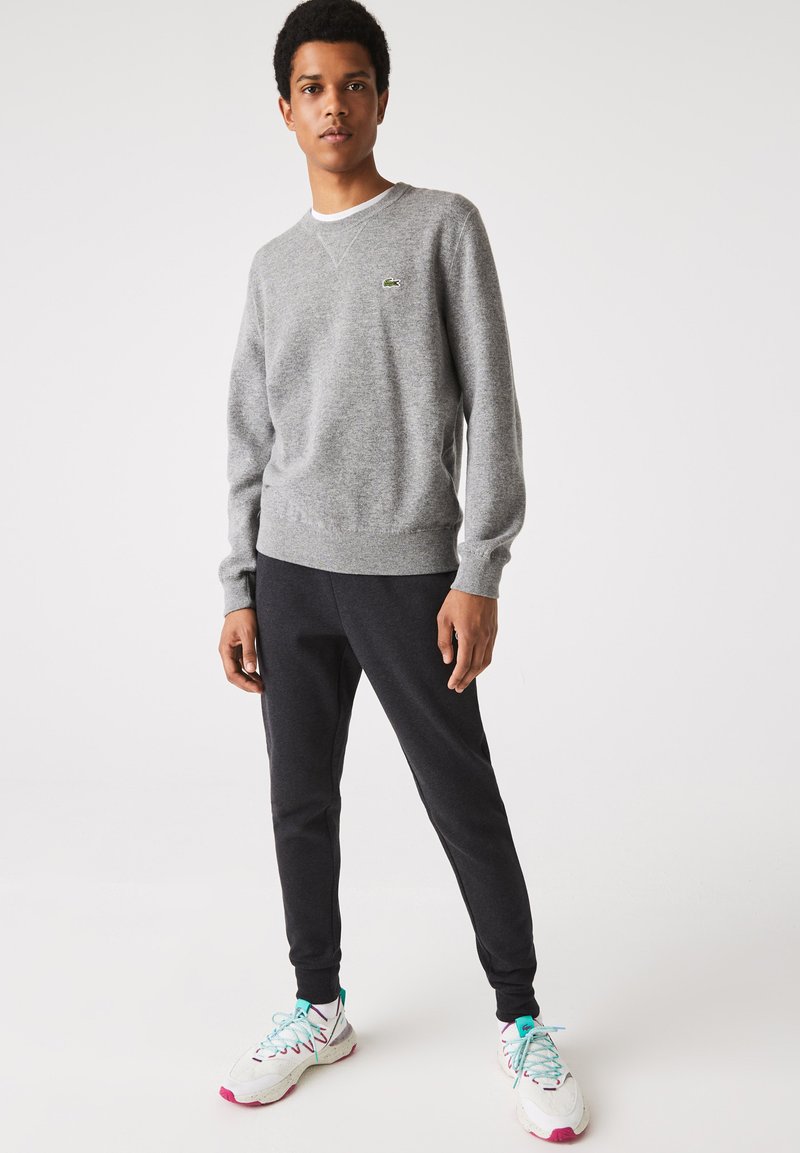 Maglione grigio in cotone con colletto a girocollo e polsini a costine, abbinato a pantaloni jogger scuri e sneakers bianche con accenti rosa.