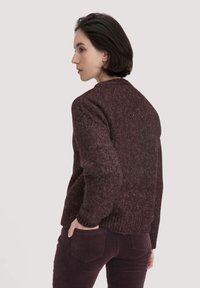 Bordeauxfarbener Strickpullover mit strukturierter Oberfläche, Rundhalsausschnitt und lockerer Passform, kombiniert mit dunklen Cordhosen.