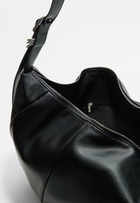 Schwarze Handtasche aus Leder mit einer großen, mit Reißverschluss versehenen Öffnung, die eine glatte Textur und einen einzelnen verstellbaren Träger hat. Innentasche sichtbar.