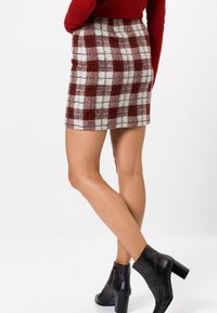Jupe mini en tartan dans un mélange de laine rouge, blanc et gris, avec une silhouette ajustée et une taille haute. Bottines noires à talons épais.