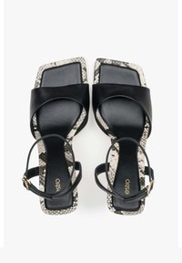 Zwarte leren blockhak sandalen met twee brede banden, een delicate enkelband en een gestructureerd slangenprintpatroon op de hak.