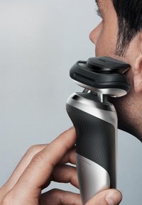 Rasoir électrique au design ergonomique noir et argent, avec une prise en main lisse et texture pointillée, et une tête arrondie pour un rasage précis.