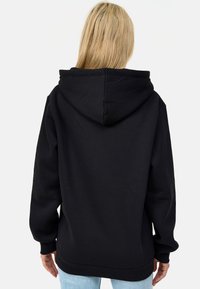 Černá mikina s volným střihem, velkou kapucí, žebrovanými manžetami a lemem. Hladká textura látky; zobrazen pohled zezadu.