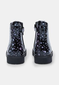 Botas de tobillo de charol negro con un patrón de corazones en púrpura y azul, que cuentan con un cierre lateral y una suela de goma texturizada.