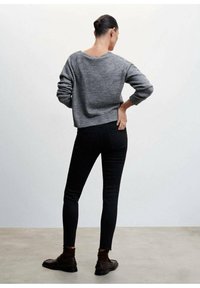 Suéter de punto gris con un escote amplio, combinado con jeans negros ajustados. Zapatos marrones y calcetines marrones texturizados completan el conjunto.