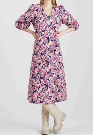 Bloemenmidi-jurk met roze, marineblauwe en witte tinten, met pofmouwen en een diepe V-hals. Gecombineerd met beige kniehoge laarzen.