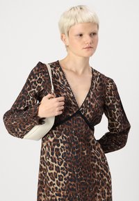 Vestido com estampa de leopardo, mangas bufantes longas, decote em V profundo e bainha de renda. A modelo segura uma pequena bolsa em tom creme.