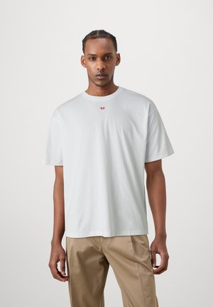 T-shirt en coton blanc avec une coupe décontractée, présentant un petit logo rouge sur la poitrine. Manches courtes et encolure ronde.