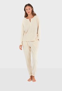 Ensemble de loungewear crème comprenant un haut à manches longues avec un col henley et un pantalon de pyjama à motifs. Tissu doux et confortable.