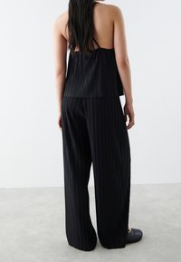 Svart plisserad halterneck-top och vida byxor set, med vertikala ränder, slät textur och avslappnad passform. Detaljer inkluderar tunna remmar och en flödande silhuett.