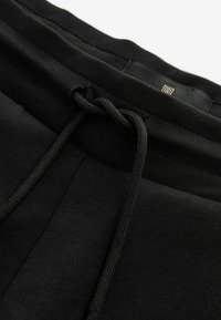 Pantalones jogger de algodón negros con cintura elástica, que presentan un cierre de cordón y una textura suave. El diseño incluye detalles de costura mínimos.