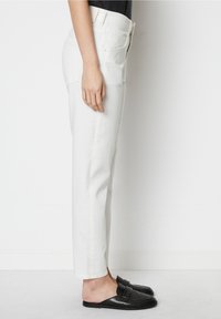 Vita denimbyxor med rak passform, hög midja och fem fickor. Kombinerat med svarta slip-on skor med en rosettdetalj.