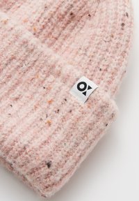 Roze gebreide muts van gestructureerde wol met spikkels van oranje en bruin. Beschikt over een wit label met een zwart logo aan de zijkant.