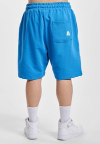 Pantaloni scurți din bumbac albastru cu talie elastică, având o buzunare pe spate cu un logo alb în formă de frunză. Textură netedă, design până la genunchi.