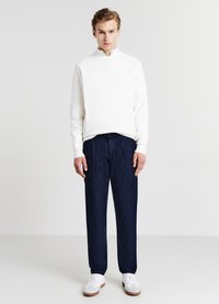 Pullover bianco a costine con colletto alto, abbinato a jeans tapered blu scuro e sneakers bianche. Design minimalista con una silhouette pulita.