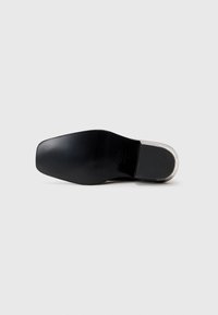 Semelle de chaussure noire au fini lisse, dotée d'un bout arrondi et d'un accent de talon transparent. Texture mate et design minimal.