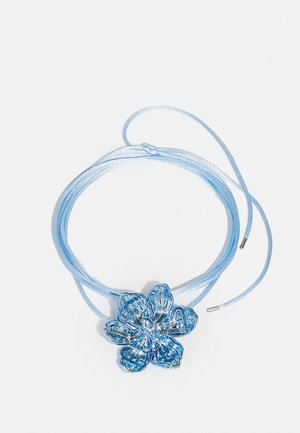 Modrá náhrdelník v tvare kvetu s lesklým povrchom, zdobený zložitými detailami lístkov, na zodpovedajúcej modrej saténovej šnúrke s kovovými koncami.