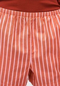 Σορτς με ελαστική μέση και κάθετες ροζ και πορτοκαλί ρίγες, φορεμένα με ριμπ κορυφή σκούρου πορτοκαλί χρώματος.