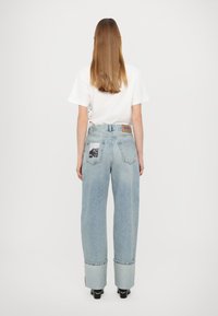 Calças de ganga de denim azul claro com um corte descontraído, punhos dobrados e dois bolsos traseiros com distintivos apliques gráficos e uma etiqueta de couro com marca.